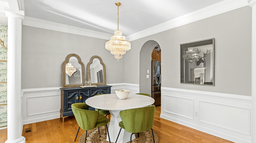 Bright dining room with a round table, green chairs, mirrors, and chandelier.